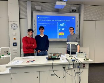 Drei Studenten der TUM stehen vor einer Tafel, die eine Präesntation zum Thema Educational Kit zur Anwendung der Lorentzkraft in der Raumfahrt zeigt