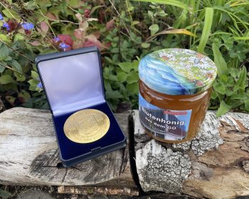 Das Bild zeigt die Medaille und ein Glas des ausgezeichneten Honigs.